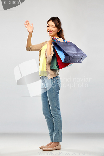 Image of happy asian woman with shopping bags waving hand