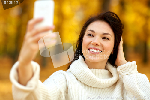 Image of woman taking selfie by smartphone at autumn park