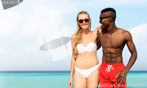 Image of mixed race couple walking along beach with friends