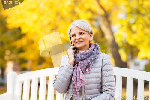 Image of senior woman calling on smartphone at autumn park