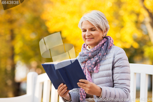 Image of happy senior woman reading book at autumn park