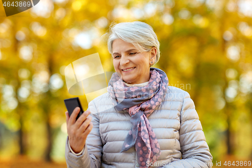 Image of happy senior woman with smartphone at autumn park