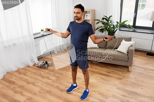 Image of indian man exercising with jump rope at home