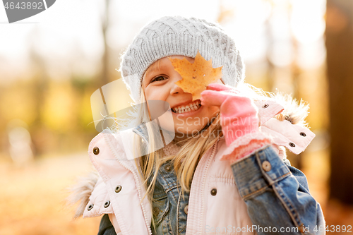 Image of happy little girl with maple leaf at autumn park