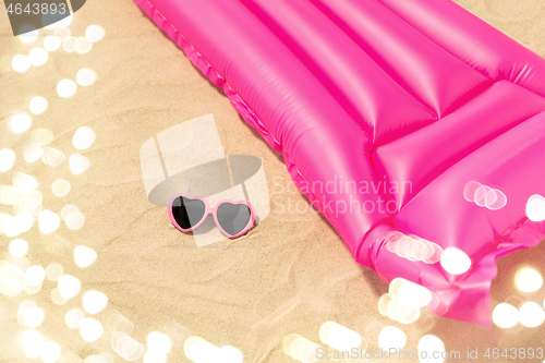 Image of sunglasses and pink swimming mattress on beach