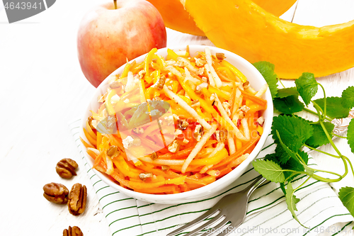 Image of Salad of pumpkin and apple with nuts in bowl on light board