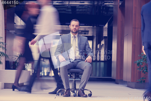 Image of business man sitting in office chair, people group  passing by