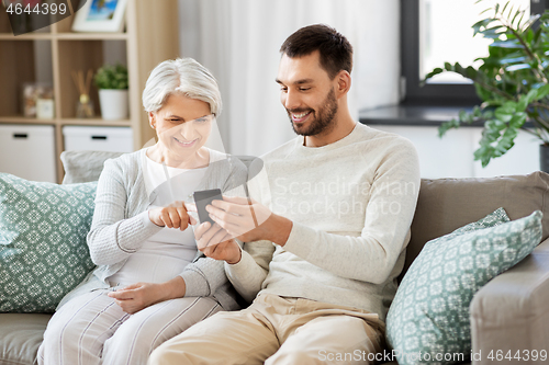 Image of old mother and adult son with smartphone at home