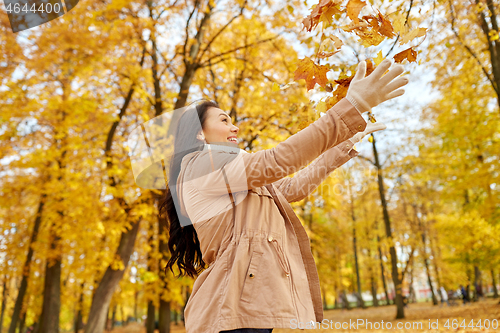 Image of happy woman having fun with leaves in autumn park