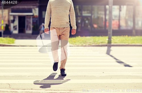 Image of senior man walking along city crosswalk