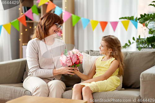 Image of granddaughter giving grandmother flowers at home