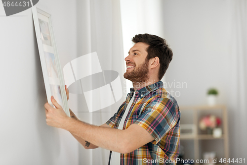 Image of man hanging picture in frame to wall at home