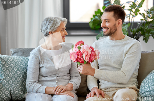 Image of adult son giving flowers to senior mother at home