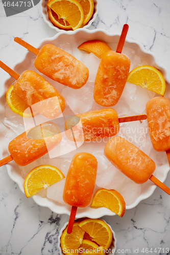 Image of Homemade, juicy, orange popsicles. Placed on a white plate with ice cubes