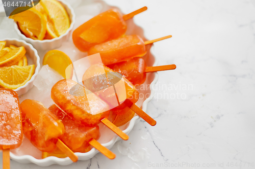 Image of Homemade, juicy, orange popsicles. Placed on a white plate with ice cubes