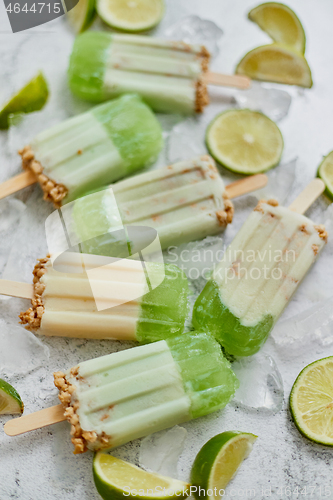 Image of Lime and cream homemade popsicles or ice creams placed with ice cubes on gray stone backdrop