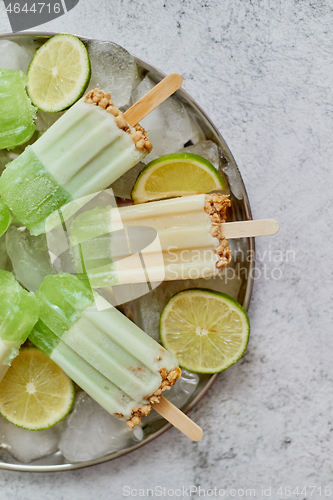 Image of Summer refreshing homemade lime popsicles with chipped ice over stone background