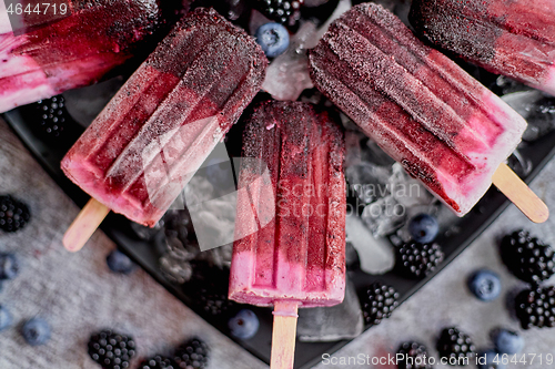 Image of Homemade fresh frozen blueberry and blackberry popsicles on black plate with ice sitting on stone