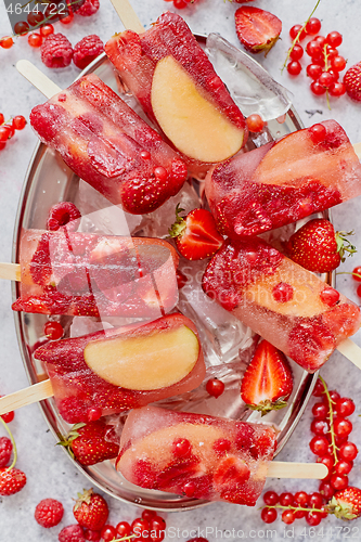 Image of Homemade raspberry, strawberry, apple and currant popsicles on metal plate with ice assorted berries