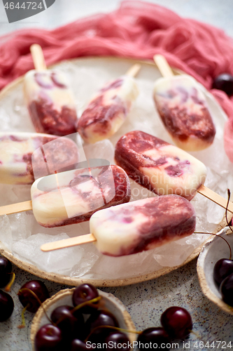 Image of Fresh cream and cherry homemade popsicles placed on white ceramic plate with fruits and textile