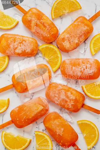 Image of Homemade frozen popsicles made with oragnic fresh oranges placed with ice cubes on marble table