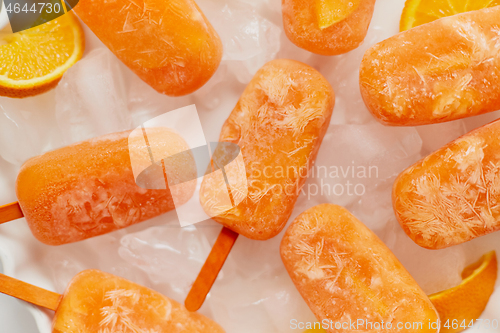 Image of Homemade frozen popsicles made with oragnic fresh oranges placed with ice cubes on marble table