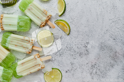 Image of Lime and cream homemade popsicles or ice creams placed with ice cubes on gray stone backdrop