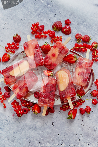 Image of Homemade raspberry, strawberry, apple and currant popsicles on metal plate with ice assorted berries