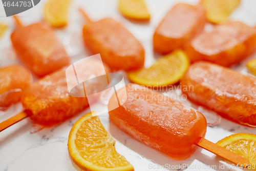 Image of Homemade frozen popsicles made with oragnic fresh oranges placed with ice cubes on marble table