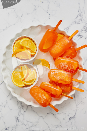 Image of Homemade, juicy, orange popsicles. Placed on a white plate with ice cubes