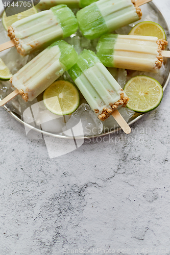 Image of Lime and cream homemade popsicles or ice creams placed with ice cubes on gray stone backdrop