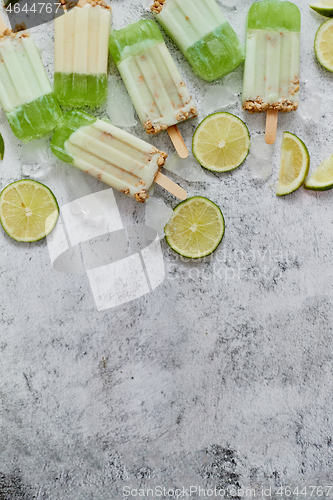 Image of Lime and cream homemade popsicles or ice creams placed with ice cubes on gray stone backdrop