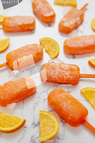 Image of Homemade frozen popsicles made with oragnic fresh oranges placed with ice cubes on marble table