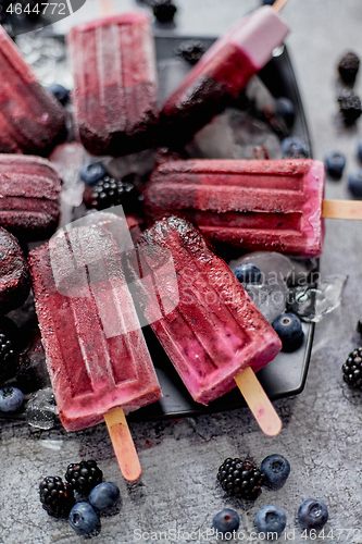 Image of Homemade fresh frozen blueberry and blackberry popsicles on black plate with ice sitting on stone