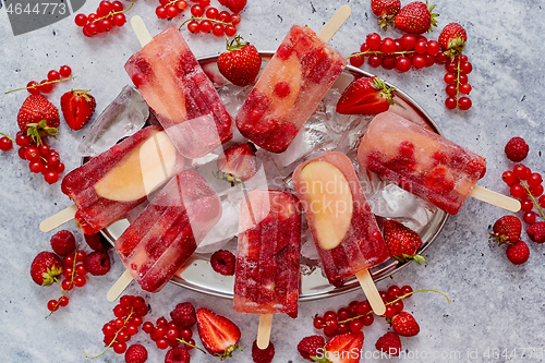 Image of Homemade raspberry, strawberry, apple and currant popsicles on metal plate with ice assorted berries