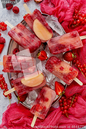 Image of Homemade raspberry, strawberry, apple and currant popsicles on metal plate with ice assorted berries