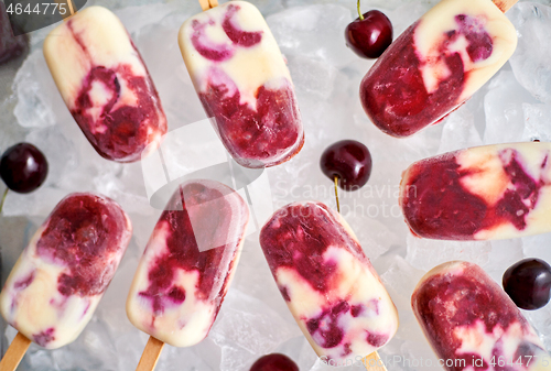 Image of Homemade, delicious, cherry and milk ice cream popsicles placed on glass tray filled with ice cubes