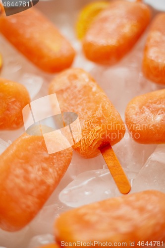 Image of Homemade frozen popsicles made with oragnic fresh oranges placed with ice cubes on marble table