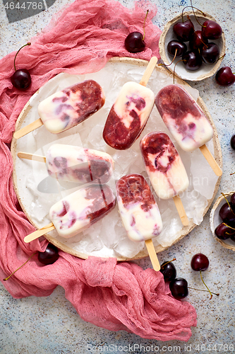 Image of Fresh cream and cherry homemade popsicles placed on white ceramic plate with fruits and textile