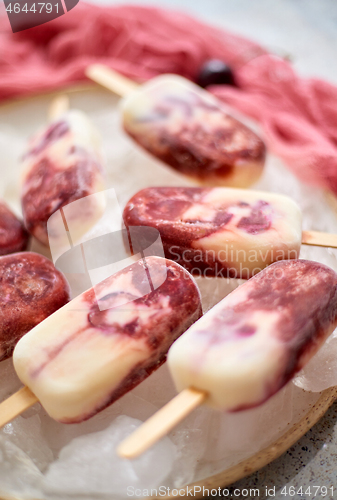 Image of Fresh cream and cherry homemade popsicles placed on white ceramic plate with fruits and textile