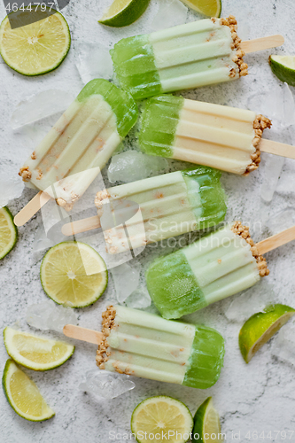 Image of Lime and cream homemade popsicles or ice creams placed with ice cubes on gray stone backdrop