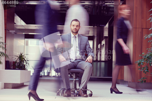 Image of business man sitting in office chair, people group  passing by