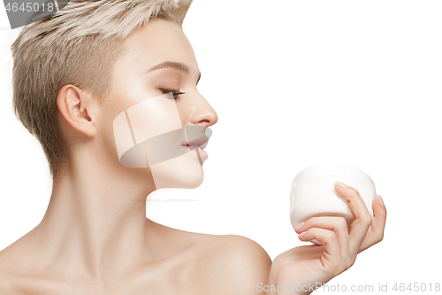 Image of Cute girl preparing to start her day. She is applying moisturizer cream on face.