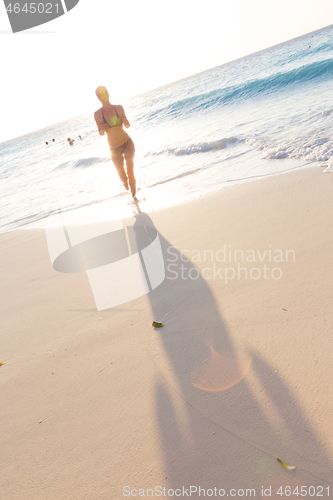 Image of Happy woman enjoying in summer, running joyfully on tropical beach in sunset. Beautiful caucasian model wearing bikini on vacations on sandy beach. Footprints in sand. Copy space