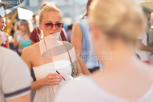 Image of It is nice to see you. It has been a while. Two happy young female friends enjoying a conversation on urban food market at random after work encounter. Pleasant free time socializing