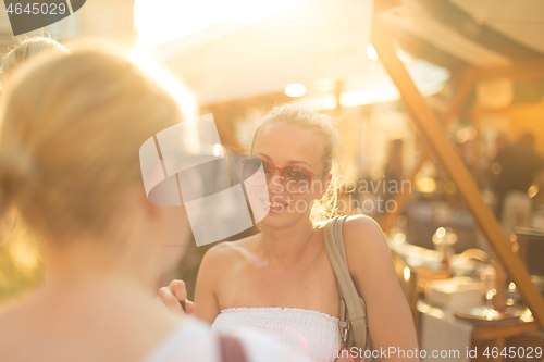 Image of It is nice to see you. It has been a while. Two happy young female friends enjoying a conversation on urban food market at random after work encounter. Pleasant free time socializing