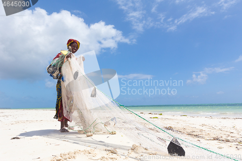 Image of Traditional african local rural fishing on Paje beach, Zanzibar, Tanzania. Traditionally dressed local woman pulling fishing net, catching small fish.