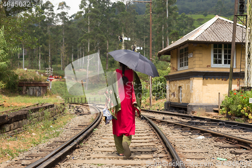 Image of Woman wearing traditional sari and black umbrella walking on railway tracks in Sri Lanka.