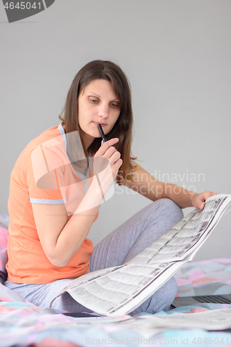 Image of Girl thoughtfully reads newspaper ads while sitting on bed at home