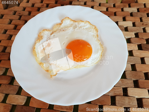 Image of Fried egg on a white plate on a wooden background